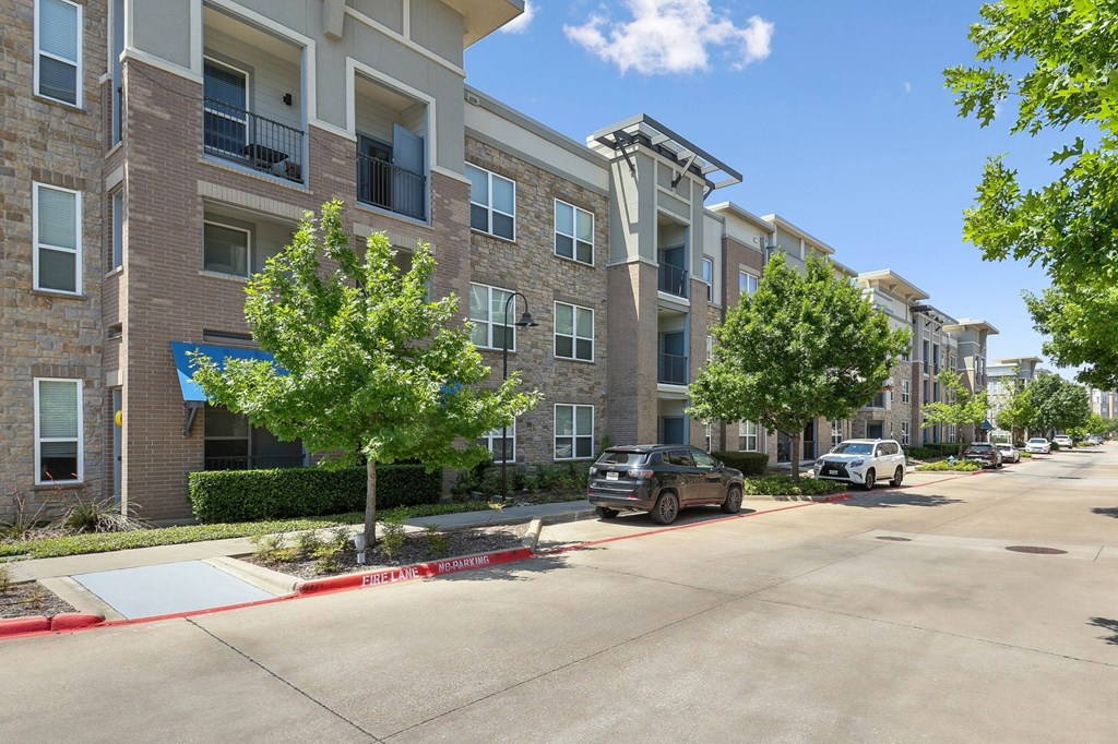 A street view of GreenVue Apartments with lush trees and street parking in Richardson, TX