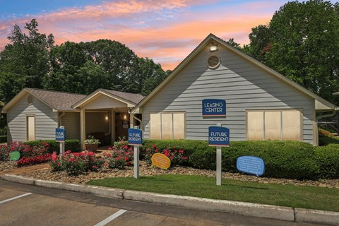 A leasing office with lush landscaping and flowers with future resident parking in front of it at Gwinnett Square Apartments in Duluth, GA