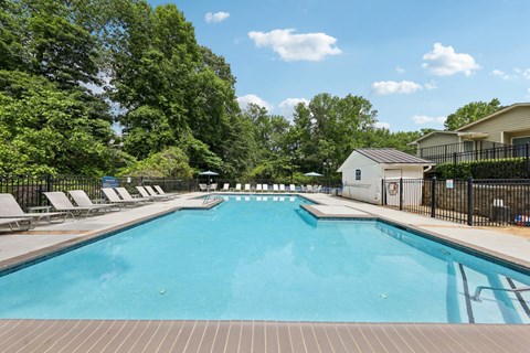 A large swimming pool surrounded by trees and lounge chairs at Gwinnett Square Apartments in Duluth, GA