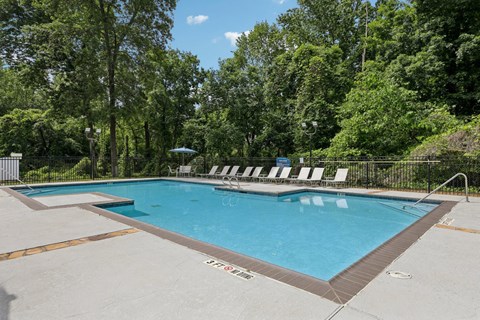 A pool with lounge chairs surrounded by lush trees at Gwinnett Square Apartments in Duluth, GA