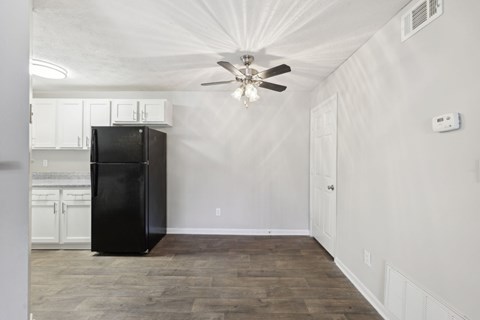 A black fridge in the kitchen leading to a dining area with a ceiling fan at Gwinnett Square Apartments in Duluth, GA