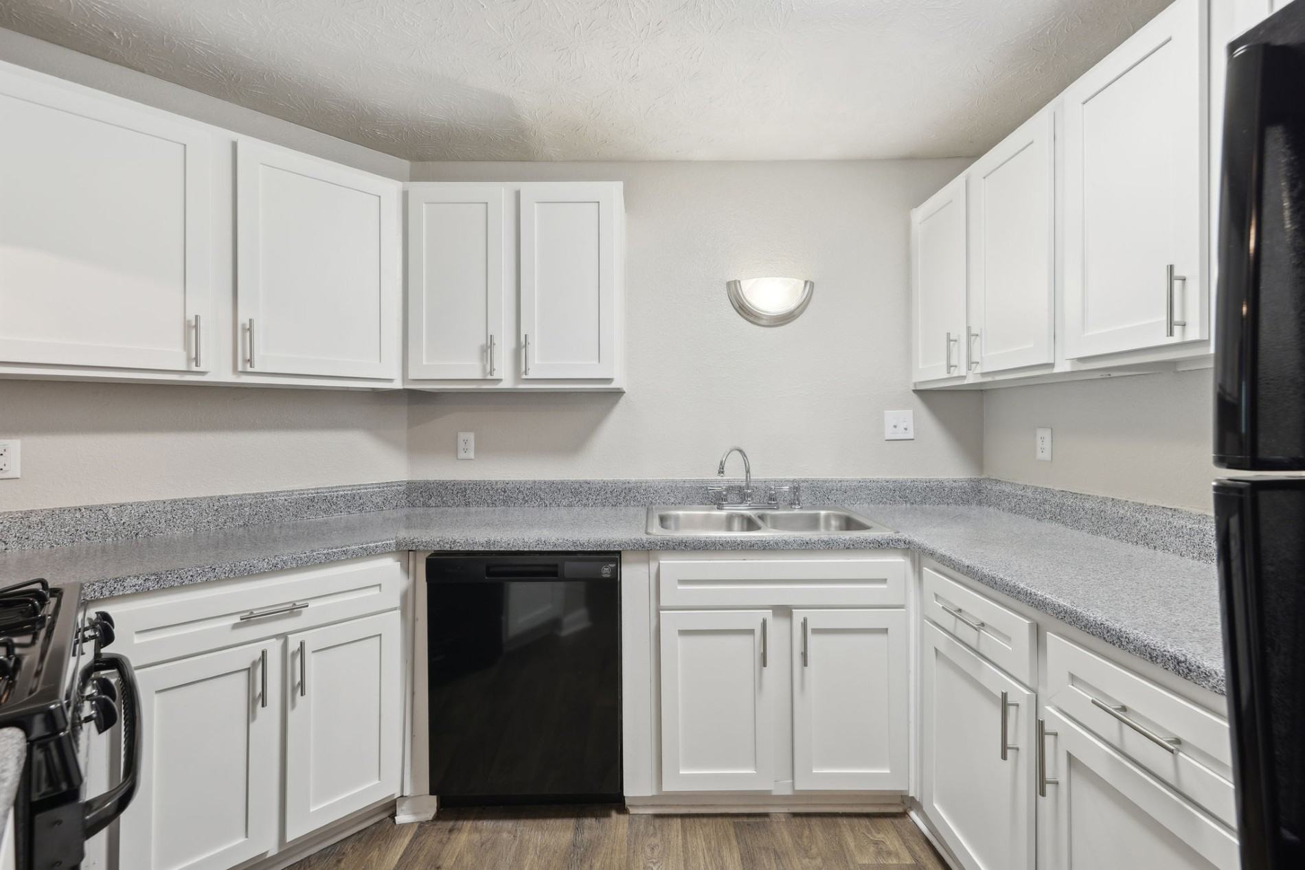 A kitchen with white cabinets and a black fridge.