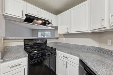 A black stove top oven in a kitchen with white cabinets at Gwinnett Square Apartments in Duluth, GA