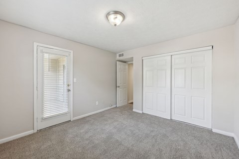 A bedroom with a carpeted floor, closet, and glass door leading to a balcony at Gwinnett Square Apartments in Duluth, GA