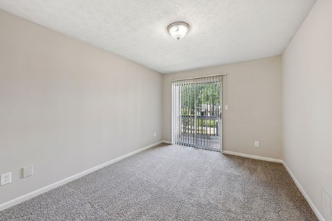 A room with a carpeted floor and a sliding glass door leading to a balcony at Gwinnett Square Apartments in Duluth, GA