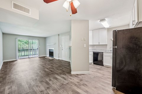 A kitchen and living area with a refrigerator, oven, and cabinets, fireplace, and glass doors leading to a balcony at Gwinnett Square Apartments in Duluth, GA