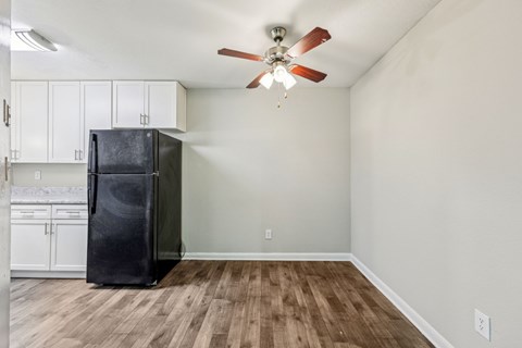 A black refrigerator is in a kitchen and dining area with white cabinets at Gwinnett Square Apartments in Duluth, GA