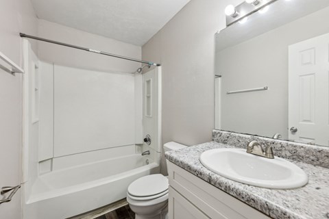 A white bathroom with a toilet, sink, mirror, and bathtub at Gwinnett Square Apartments in Duluth, GA