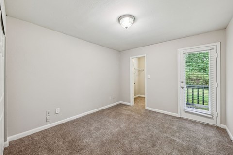 A bedroom with a carpeted floor and a door leading to a balcony at Gwinnett Square Apartments in Duluth, GA