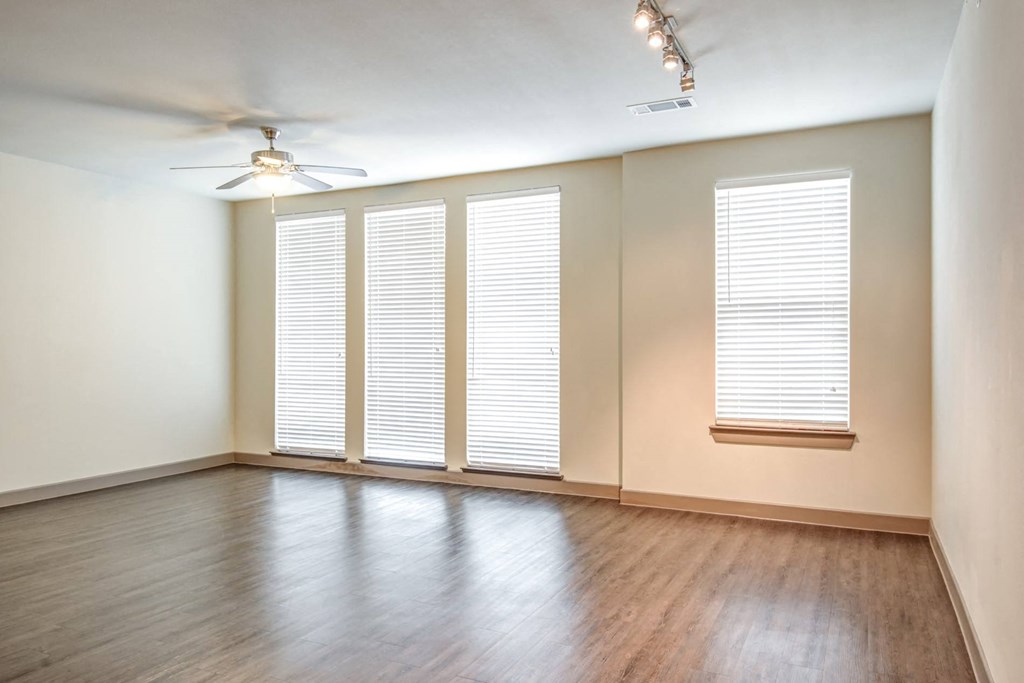 an empty living room with windows and wood floors and a ceiling fan
