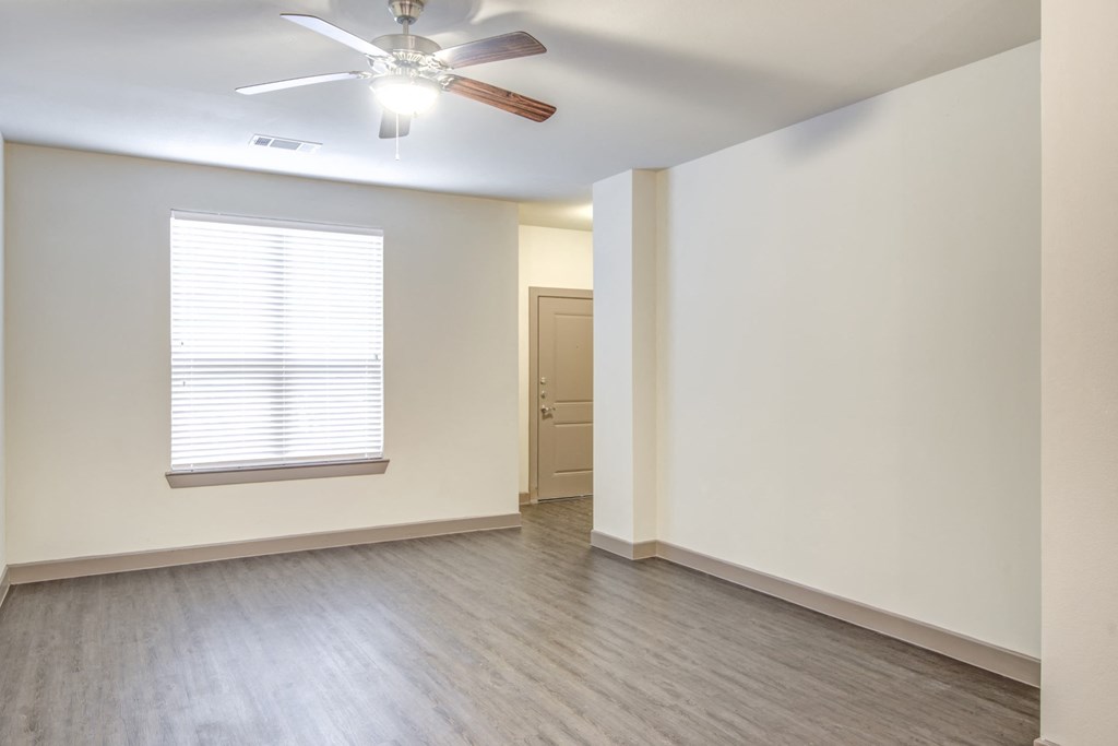 an empty living room with a ceiling fan and a window