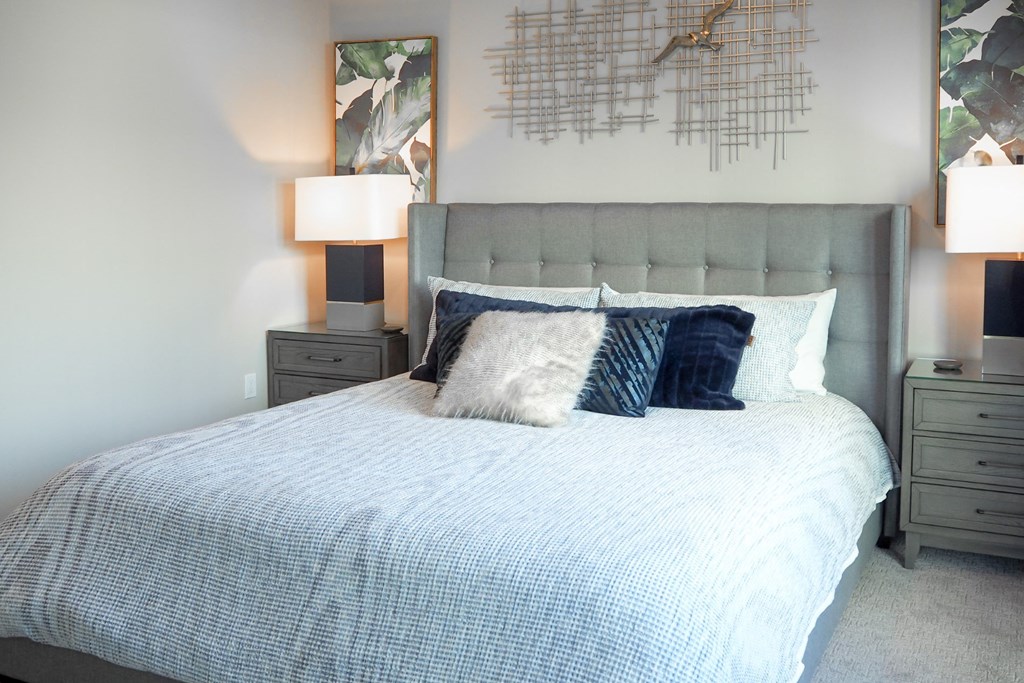3 bedroom model master bedroom with a bed with pillows and a grey headboard at The Hamilton apartments in Dallas, TX