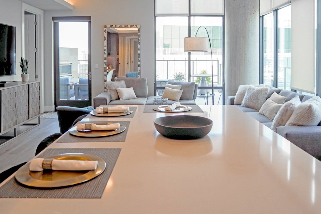 3-bedroom model view of kitchen island with the living room with couches and chairs in the background at The Hamilton apartments in Dallas, TX