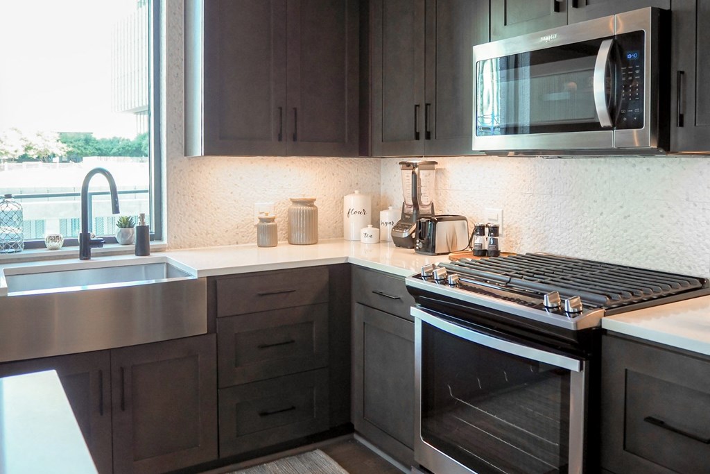 3 bedroom model kitchen with stainless steel appliances, quartz countertops, and a window at The Hamilton apartments in Dallas, TX