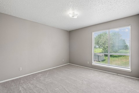 A bedroom with a window and a view of a green grass and trees outside at Heritage Square Apartments in Waco, TX