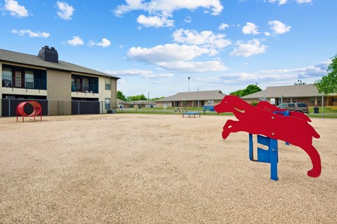 A red dog-shaped park equipment sits in the middle of a dog park at Heritage Square Apartments in Waco, TX