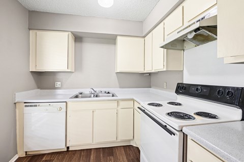 A kitchen with a white stove top oven, stainless steel sink, and a white dishwasher at Heritage Square Apartments in Waco, TX