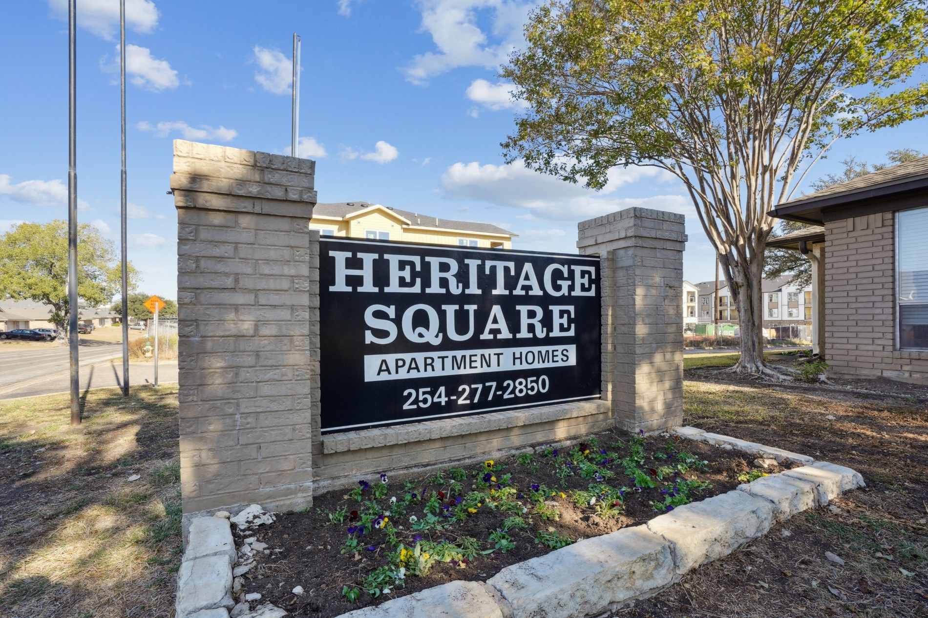 A sign for Heritage Square Apartment Homes stands in front of a building.