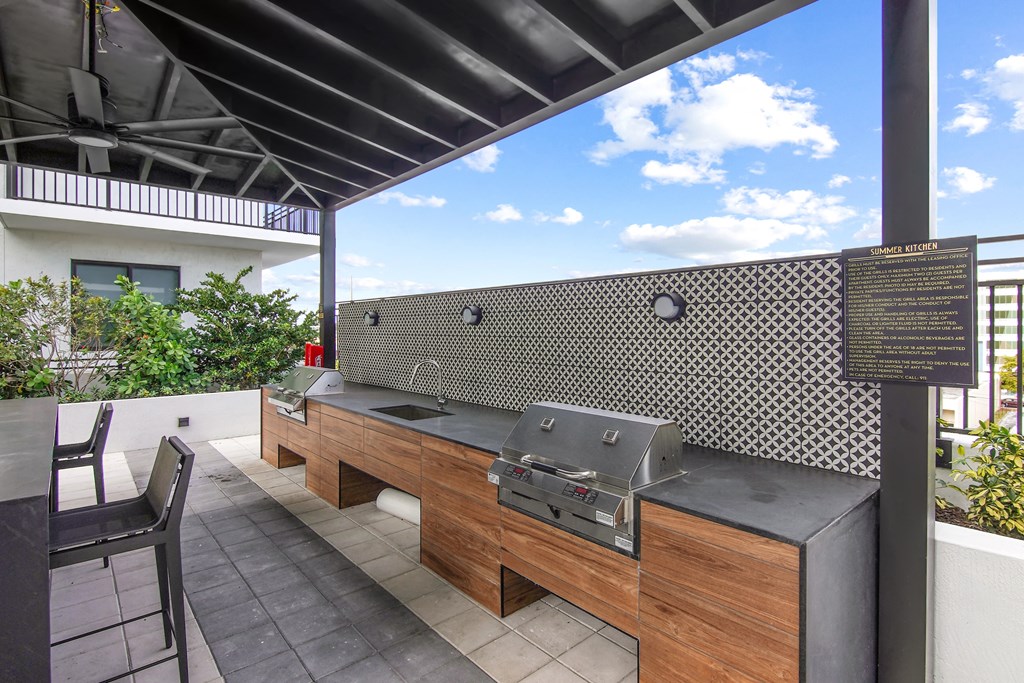 Outdoor grilling station with two BBQ grills, a sink, and ample seating under a pergola  Balcony view of Hollywood Boulevard at Hollywood Heights on the Boulevard Luxury Apartments in Hollywood, FL