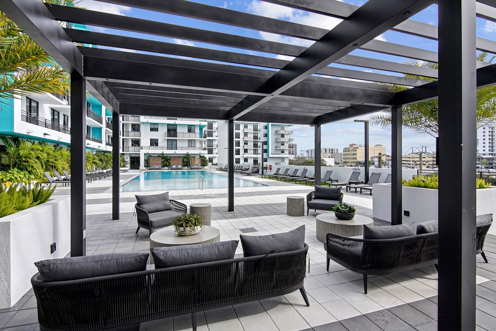 Outdoor couch seating under a pergola with our beautiful pool in the background at Hollywood Heights on the Boulevard Luxury Apartments in Hollywood, FL