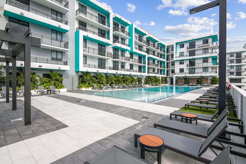 Patio lounge chairs surrounding our beautiful pool with lush greenery  at Hollywood Heights on the Boulevard Luxury Apartments in Hollywood, FL