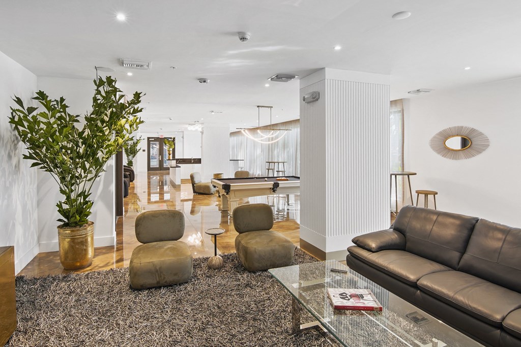 lounge area with brown chairs, a grey couch, and a green plant with our social club with a pool table in the background at Hollywood Heights on the Boulevard Luxury Apartments in Hollywood FL