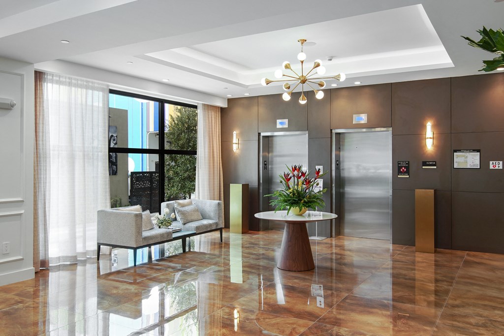 Lobby area with white table with a flower arrangement, white chairs and elevators at Hollywood Heights on the Boulevard Luxury Apartments in Hollywood, FL