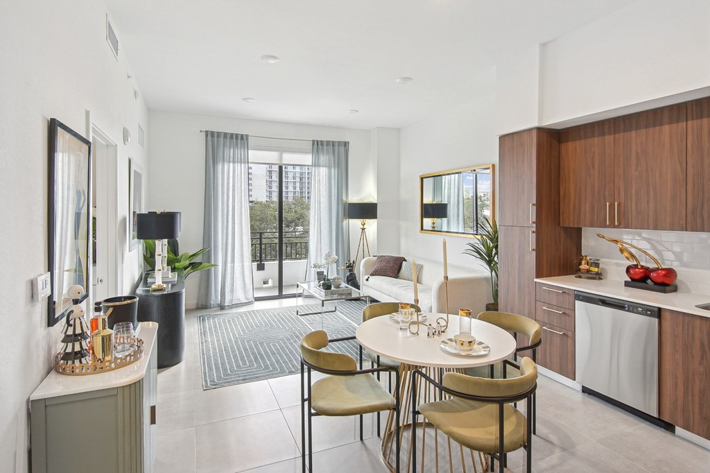 A modern dining room with a table set for two and a kitchen area with wooden cabinets. A modern kitchen with a dining table and chairs, fridge with a ice maker, stovetop, and microwave Living room and modern kitchen in our 2-bedroom model with a dining table and chairs Balcony view of Hollywood Boulevard at Hollywood Heights on the Boulevard Luxury Apartments in Hollywood, FL
