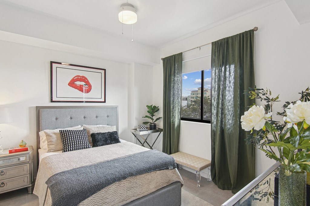 A bedroom with a large bed and a framed picture of red lips above it and a window with green curtains at Hollywood Heights on the Boulevard Luxury Apartments in Hollywood, FL