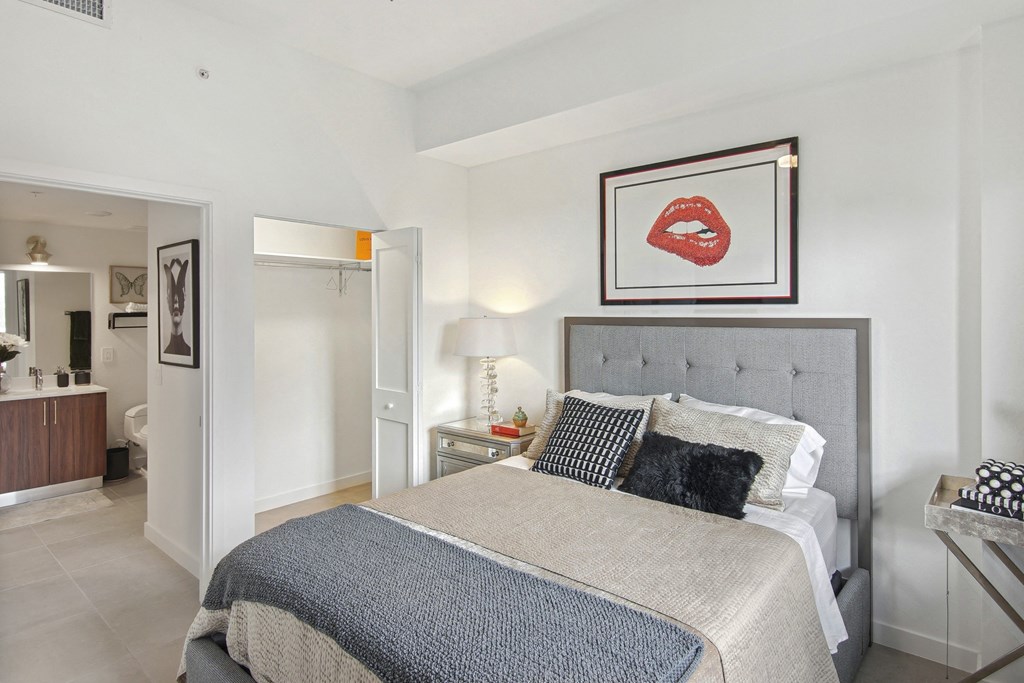 A bedroom with a bed, nightstand, and a picture of red lips above the bed at Hollywood Heights on the Boulevard Luxury Apartments in Hollywood, FL