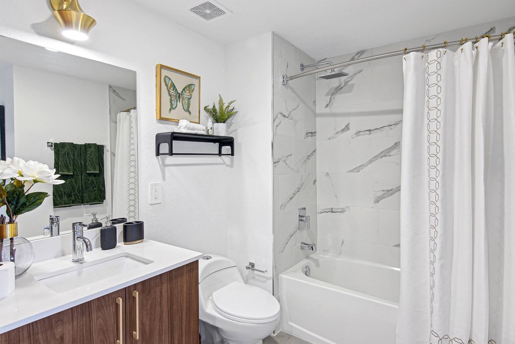 A bathroom with a marble shower, a white counter with wooden cabinets and a white toilet at Hollywood Heights on the Boulevard Luxury Apartments in Hollywood, FL