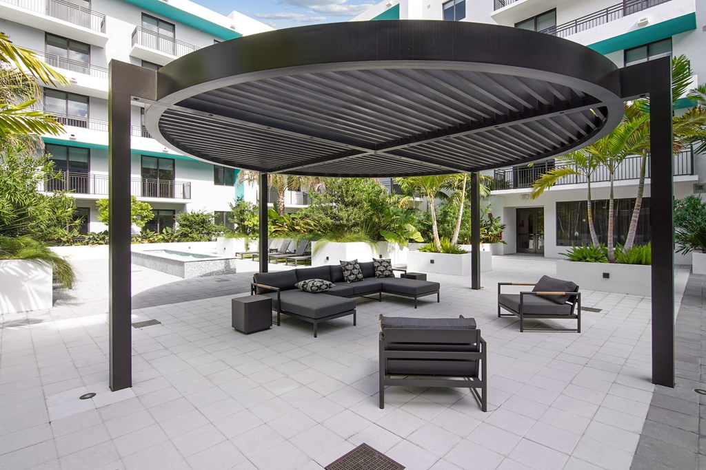 A patio with cushioned outdoor seating under a circular pergola at our courtyard at Hollywood Heights on the Boulevard Luxury Apartments in Hollywood, FL