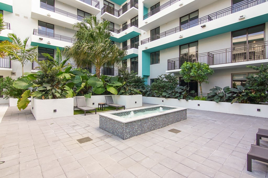 A small fountain surrounded by our serenity garden and lounge chairs at Hollywood Heights on the Boulevard Luxury Apartments in Hollywood, FL