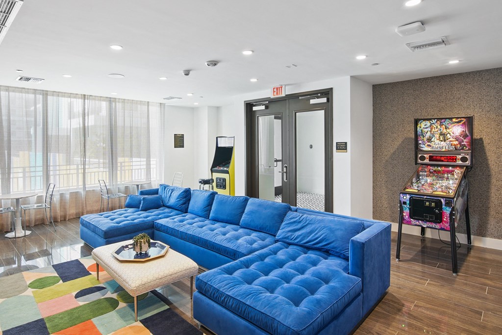 Our lounge and gaming zone with a blue sofa and arcade games at Hollywood Heights on the Boulevard Luxury Apartments in Hollywood, FL