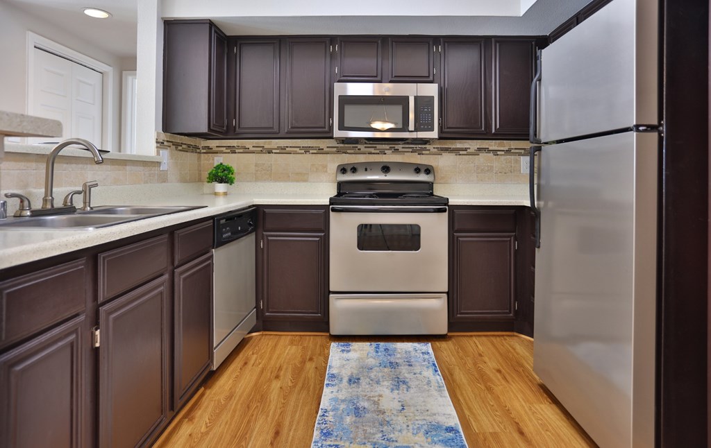 A1 kitchen with brown cabinets, wood-like floors, and stainless steel appliances at The Inverness Apartments in Houston, TX