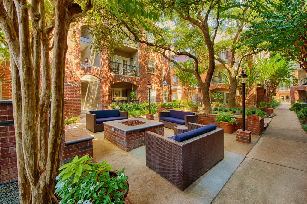 A courtyard with a fire pit and chairs surrounded by trees at The Inverness Apartments in Houston, TX