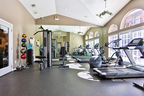 A gym with a variety of equipment including treadmills, weights, and exercise machines at The Inverness Apartments in Houston, TX