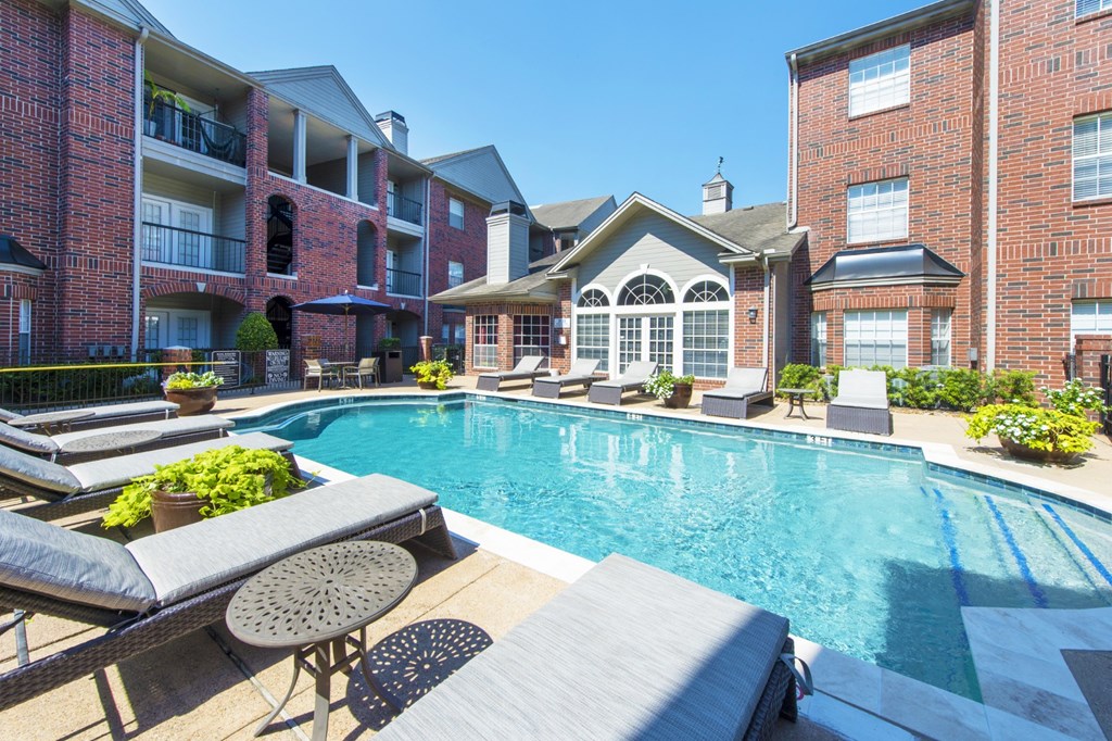 A swimming pool surrounded by lounge chairs and plants at The Inverness Apartments in Houston, TX