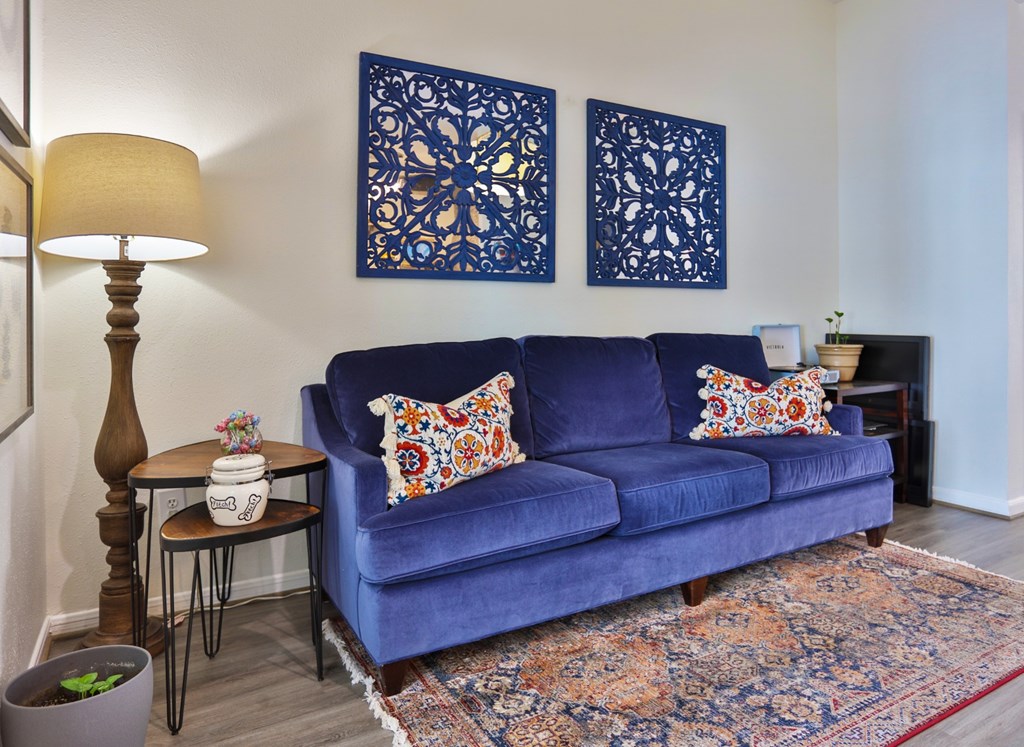 A resident lounge with a blue couch, lamp, and a side table at The Inverness Apartments in Houston, TX