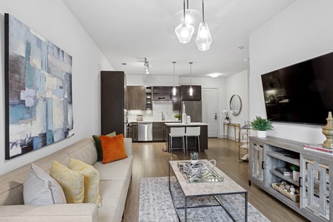 A modern living room with a large painting on the wall and a white sofa with orange and yellow pillows at Knox Heights Apartments in Dallas, TX