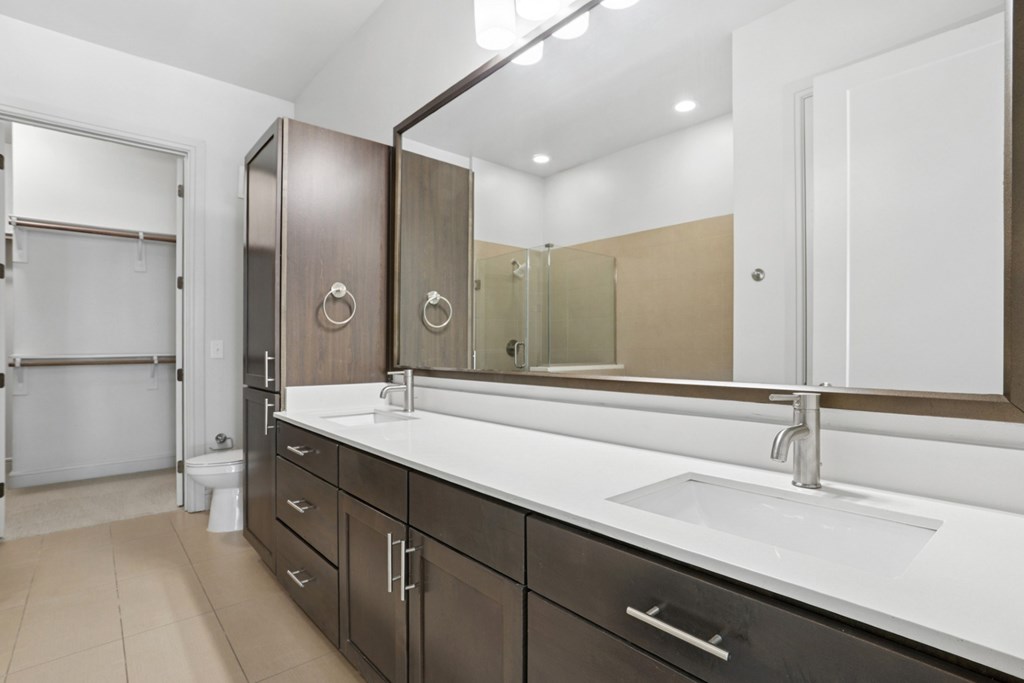 A modern bathroom with a sink, mirror, dark cabinets, and a toilet at Knox Heights Apartments in Dallas, TX