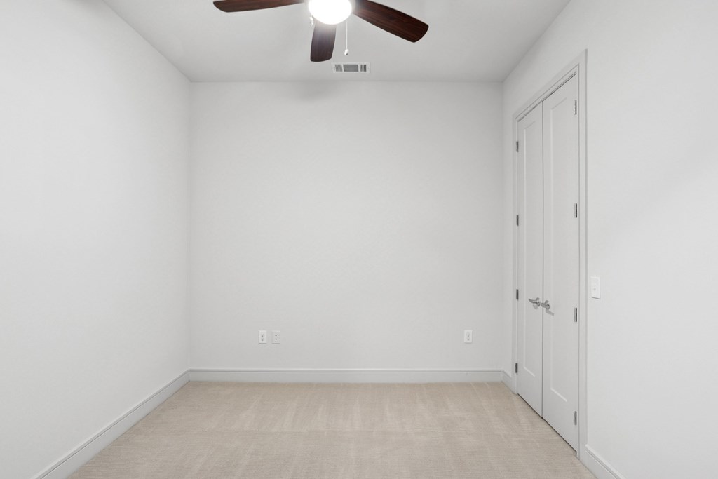 A carpeted bedroom with a ceiling fan and a door at Knox Heights Apartments in Dallas, TX