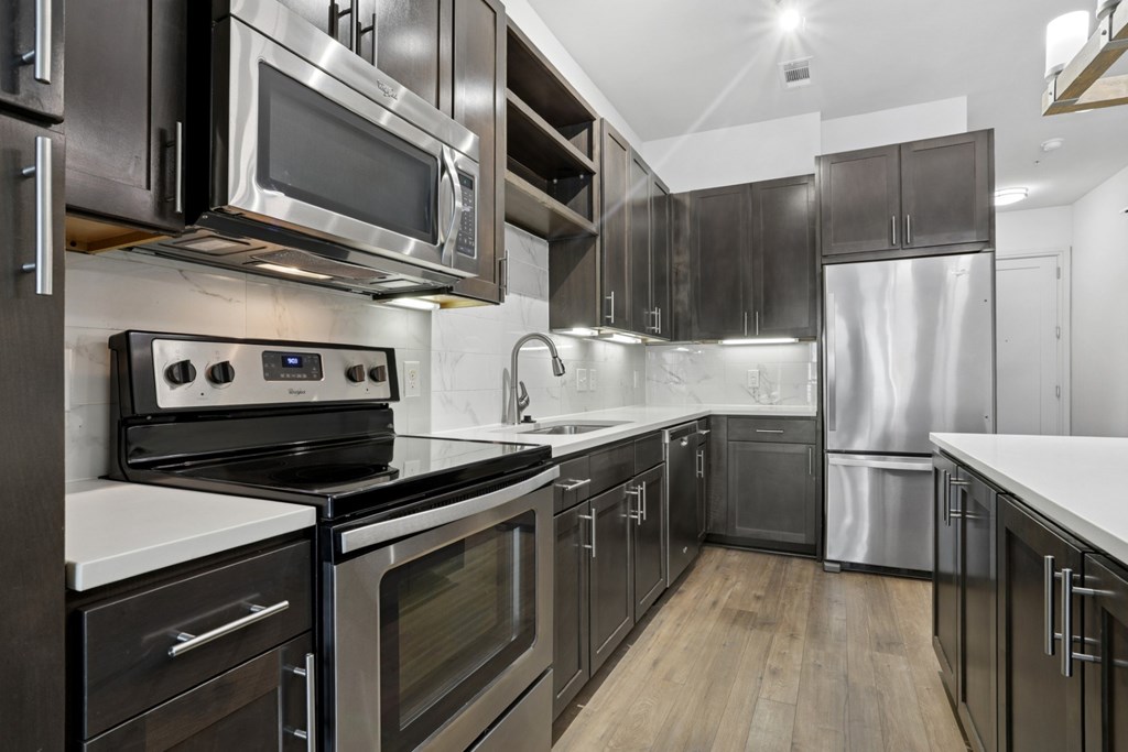 A modern kitchen with stainless steel appliances, dark cabinets, and wooden floors at Knox Heights Apartments in Dallas, TX