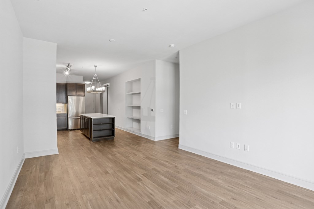 A living and dining room with white walls and wooden flooring with a kitchen area in the background at Knox Heights Apartments in Dallas, TX