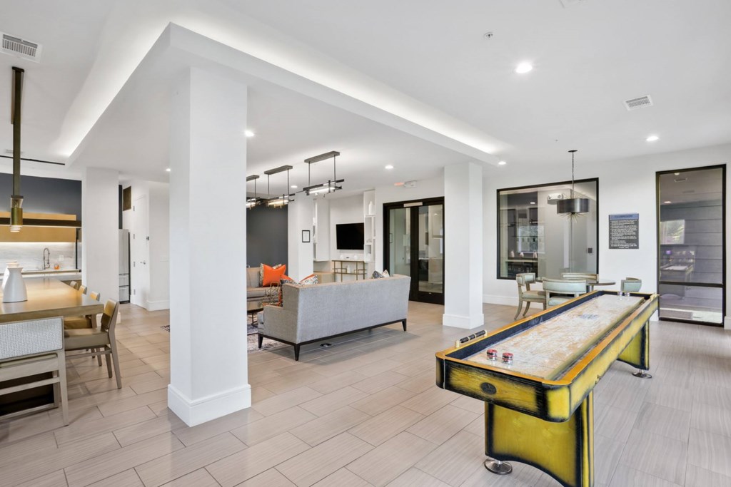 A shuffleboard table is in the middle of a spacious entertainment lounge with sofas and white walls at Knox Heights Apartments in Dallas, TX