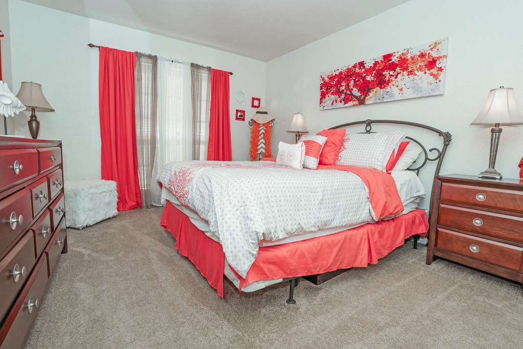 A bedroom with a large bed and red curtains at Laurel Parc apartments in Shreveport, LA.