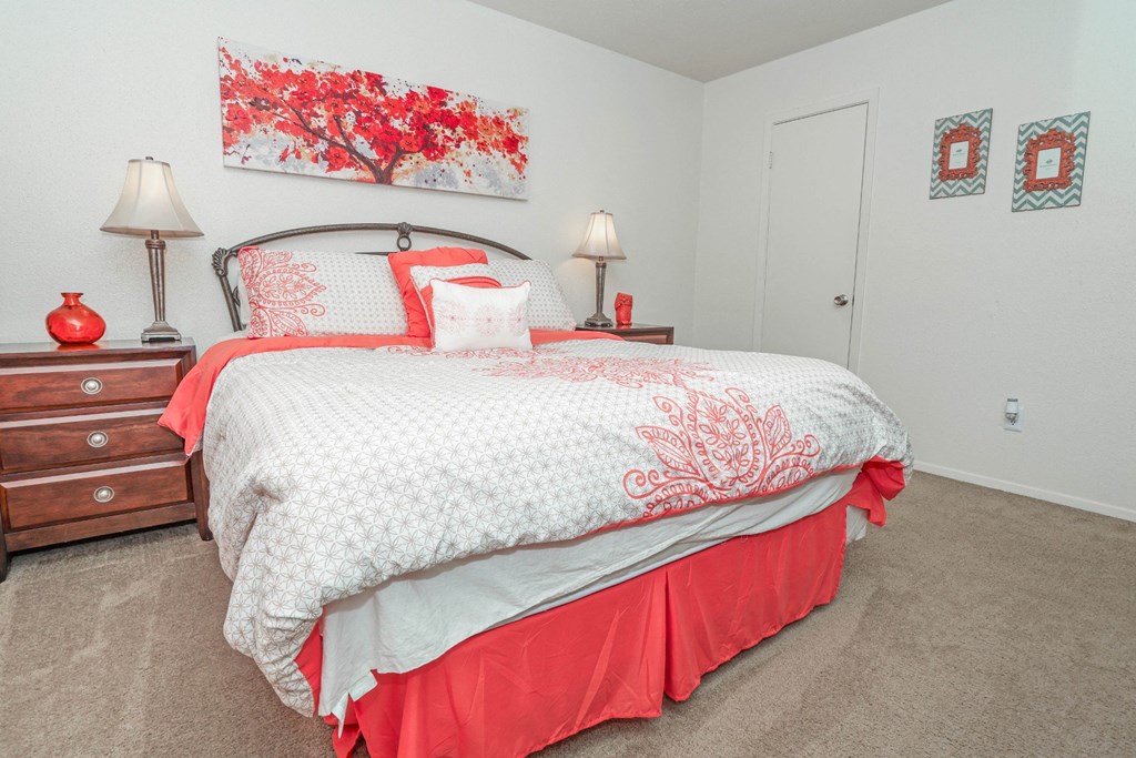 View of bed in model apartment bedroom with red painting on the wall at Laurel Parc apartments in Shreveport, LA.