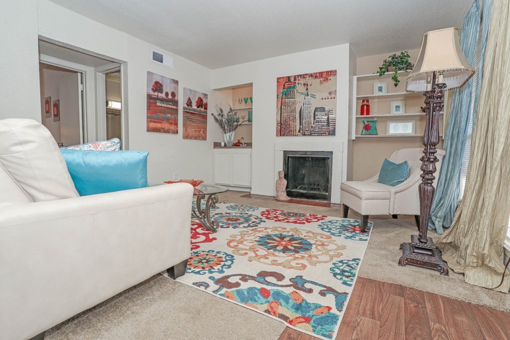 Large model living room with a white couch and a colorful rug facing a fireplace at Laurel Parc apartments in Shreveport, LA.