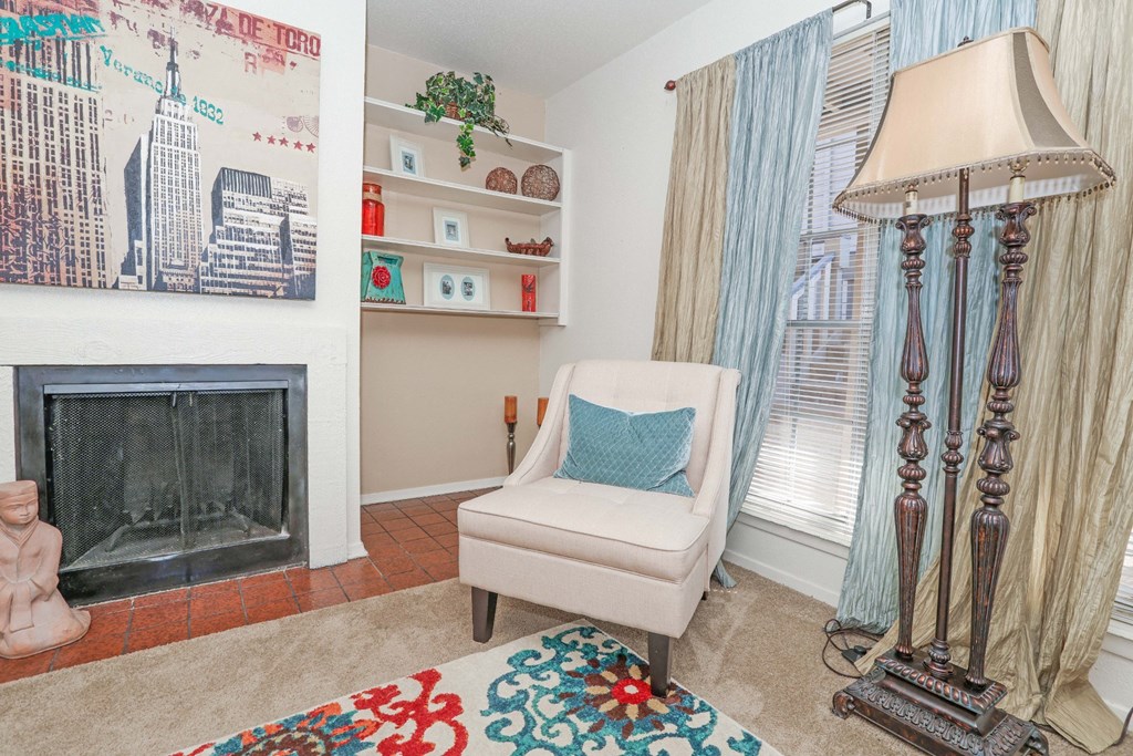 Model apartment living room with a fireplace, a chair, and a lamp at Laurel Parc apartments in Shreveport, LA.