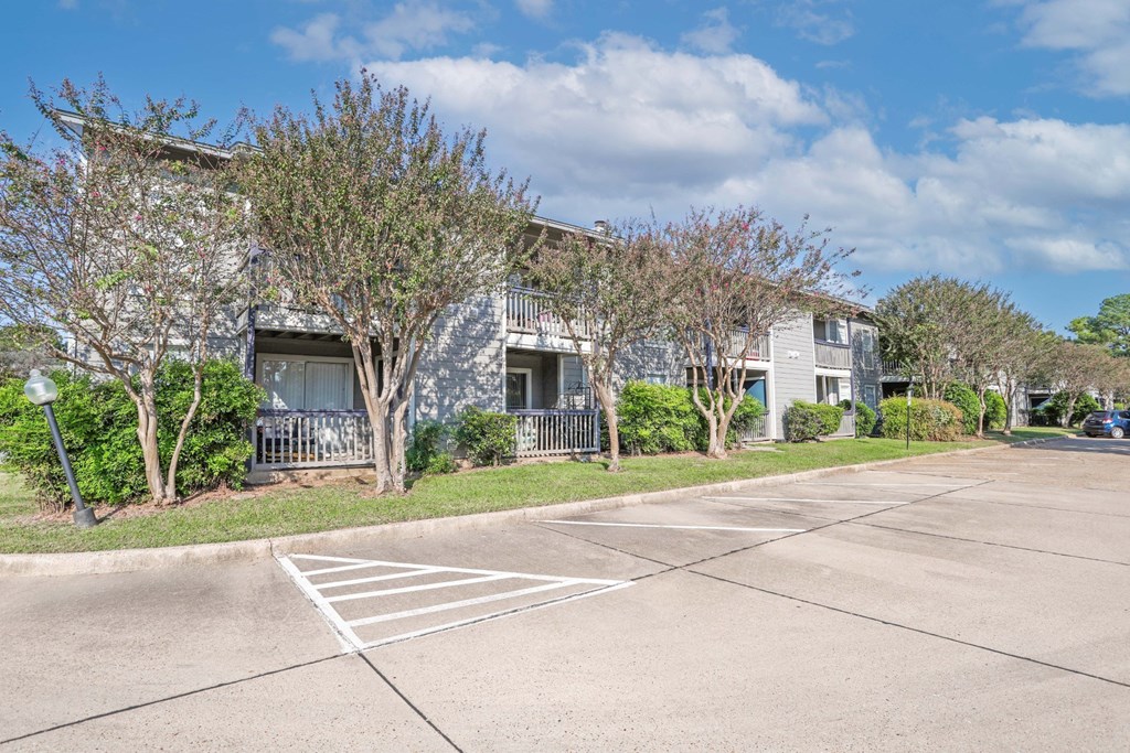 Surface parking lot in front of apartment buildings with a clear blue sky at Laurel Parc apartments in Shreveport, LA.